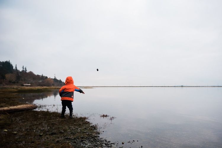 Rear view of child throwing stone in lake against sky
