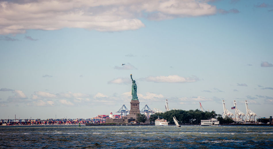 Statue of liberty in city against cloudy sky