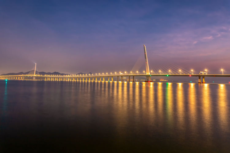 Illuminated bridge over river against sky at night