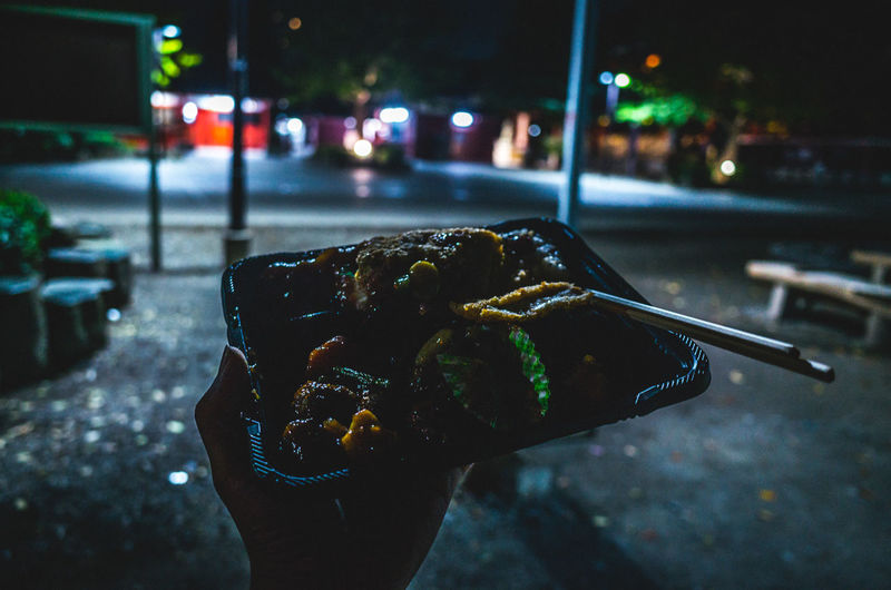 Close-up of hand holding food on street at night