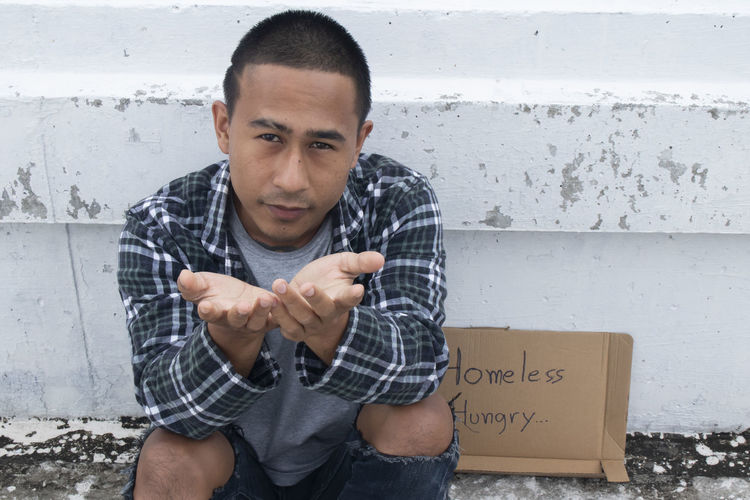Portrait of young man sitting against wall