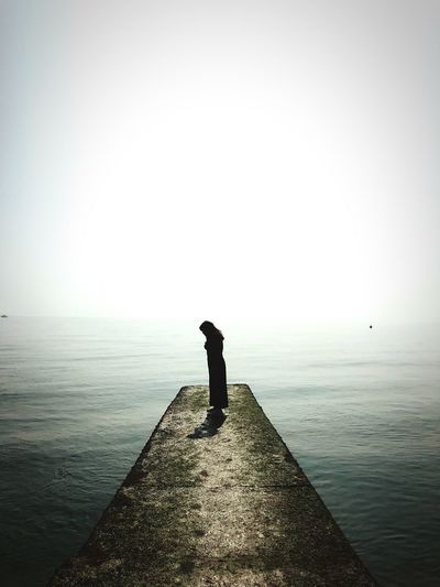 Silhouette man standing on sea against clear sky