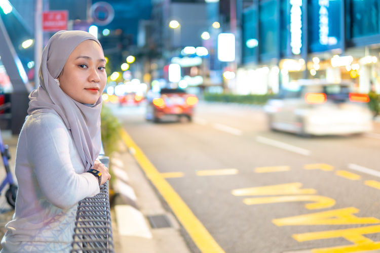 E-hailing concept, beautiful malay girl holding smartphone outdoor at the taxi stop