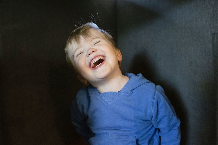 Joyful and happy toddler boy tilts head back while laughing indoors