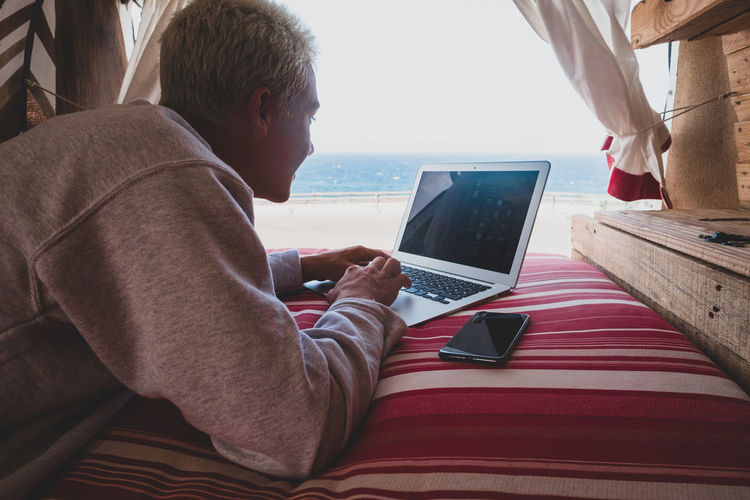 Teenager using laptop while lying on bed in motor home against sea