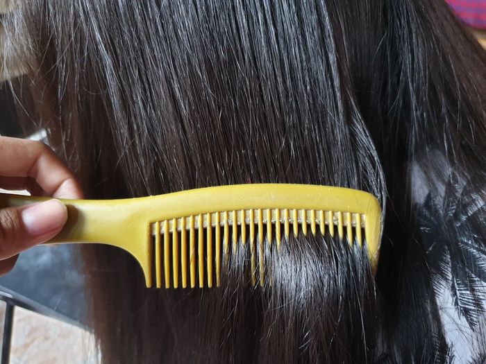 Cropped hand of person combing woman hair