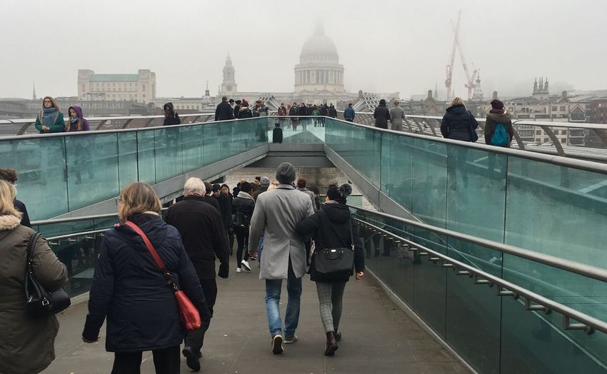 Rear view of people walking on bridge against sky