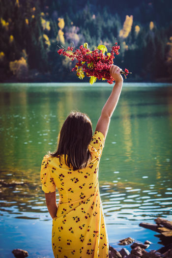 Rear view of young woman holding flowers while standing by lake
