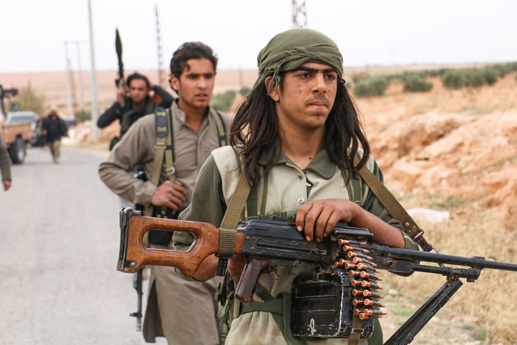 People with rifles and ammunition walking on road