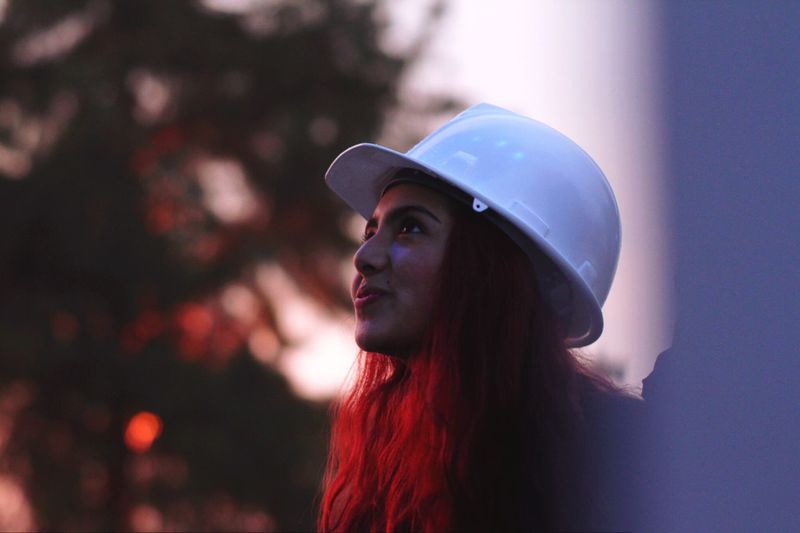 Close-up of young woman wearing hardhat during sunset