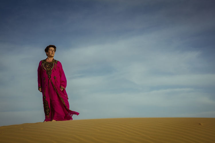 Low angle view of woman standing at desert against sky