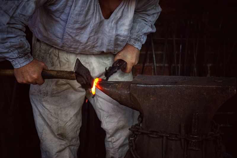 Midsection of blacksmith using hammer on anvil at workshop