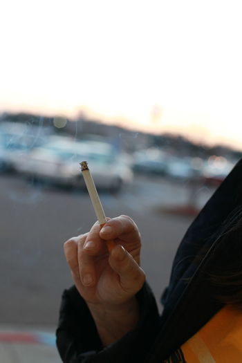 Cropped hand holding cigarette against clear sky 