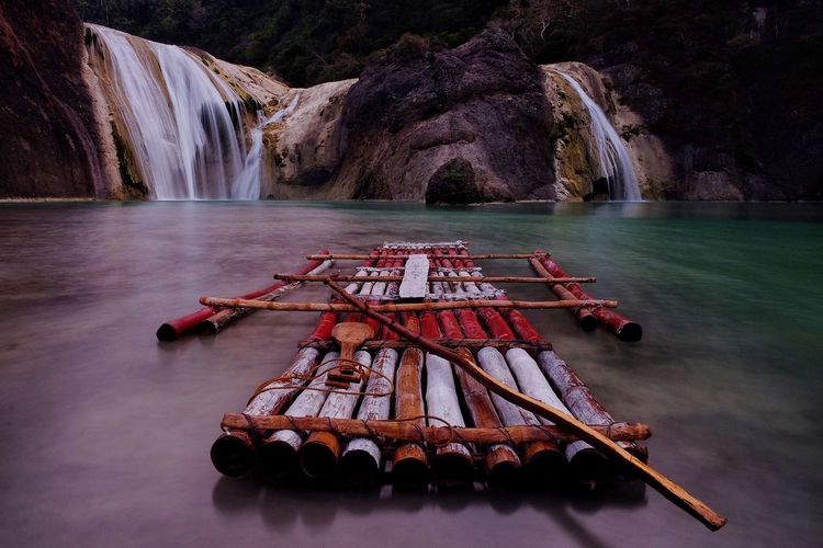 Wooden raft in river against waterfall
