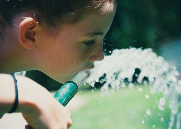 Close-up of girl drinking water from hose in yard