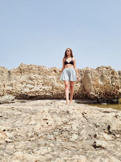 Full length of woman standing on rock against clear sky