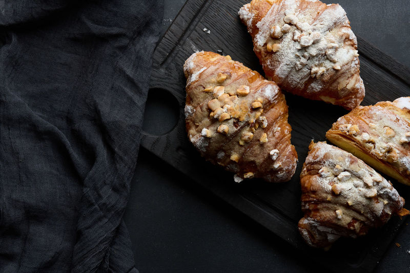 Baked croissant on a wooden board and sprinkled with powdered sugar, black table. appetizing pastri