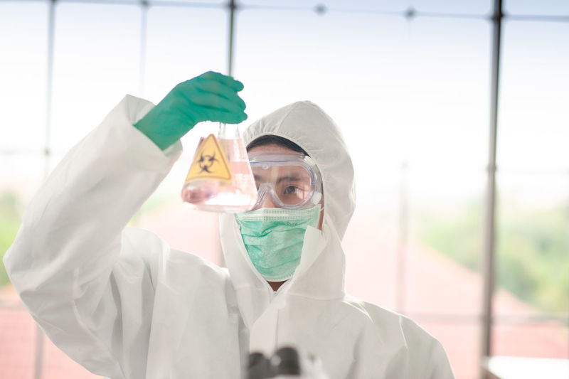 Scientist wearing protective suit holding flask at laboratory