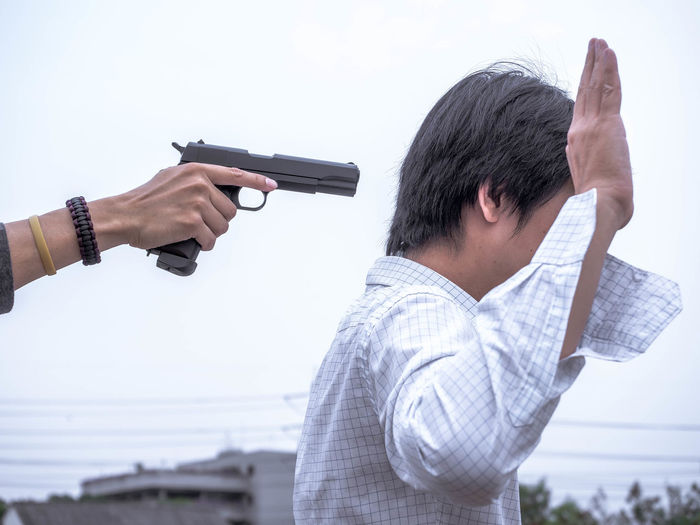 Cropped hand aiming gun on man with arm raised