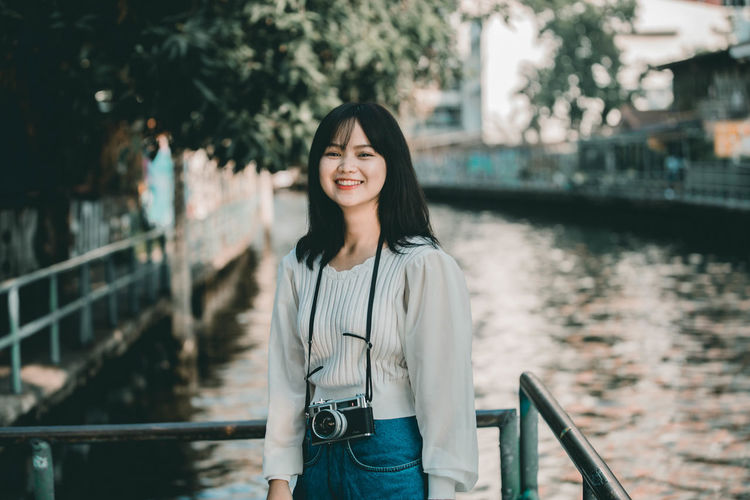 Portrait of smiling young woman standing by railing