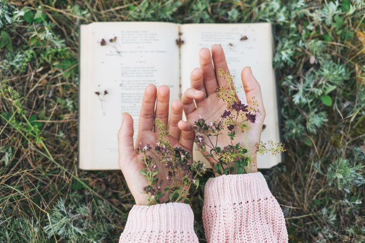 Directly above shot of woman hand with flower and book outdoors
