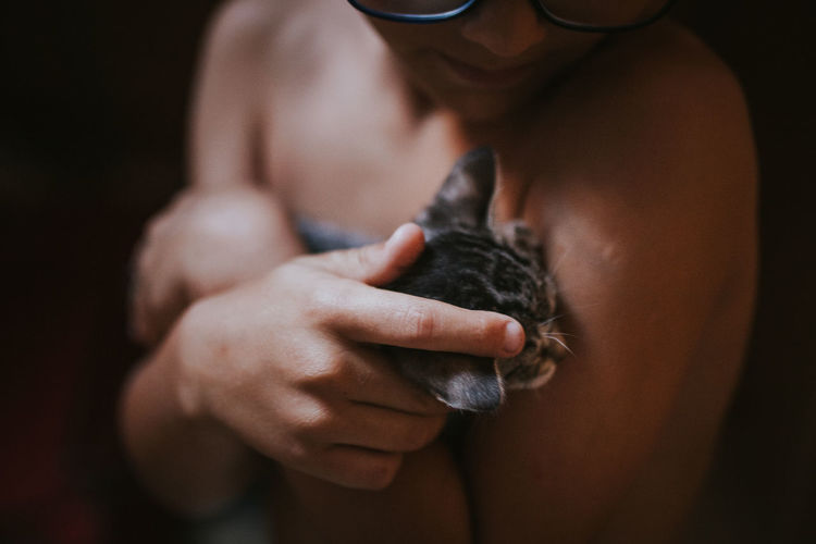Midsection of shirtless teenage boy holding cat against black background