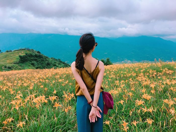 Woman standing on flowering field against mountains