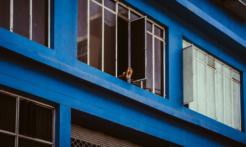 Man's feet sticking out through the window of high blue building. drying feet in the fresh air