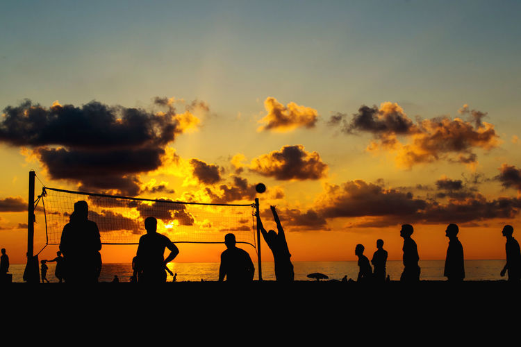Silhouette people playing volleyball at beach against sky during sunset