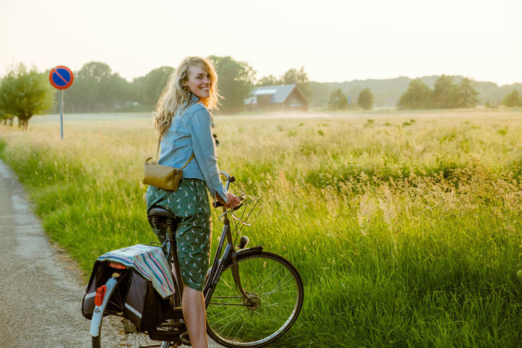 Full length portrait of happy woman with bicycle on field