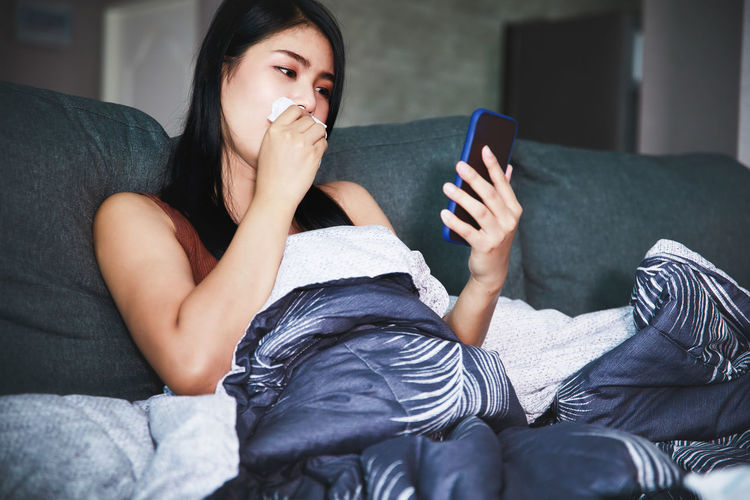 Young woman using mobile phone on sofa at home