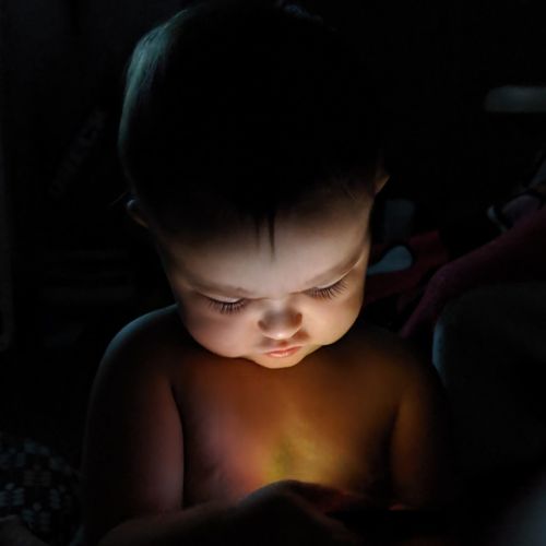 Close-up of shirtless baby girl holding mobile phone in darkroom