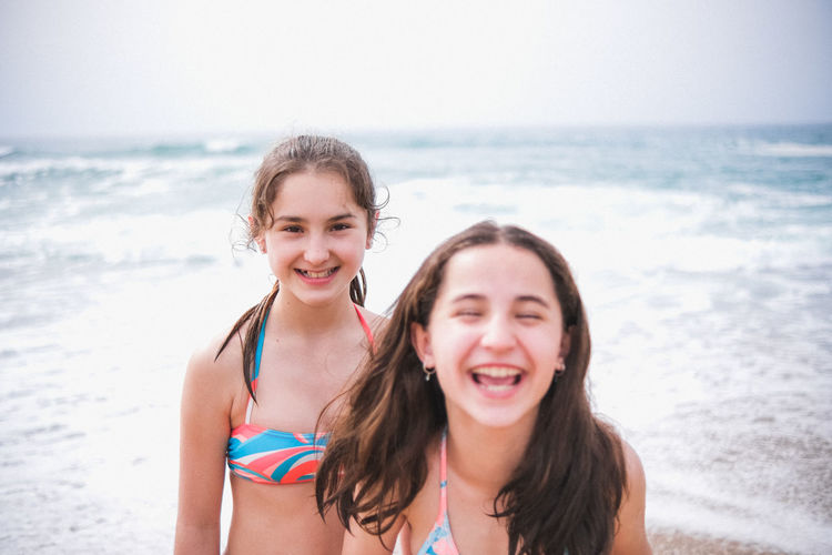 Portrait of smiling friends in bikini standing at beach