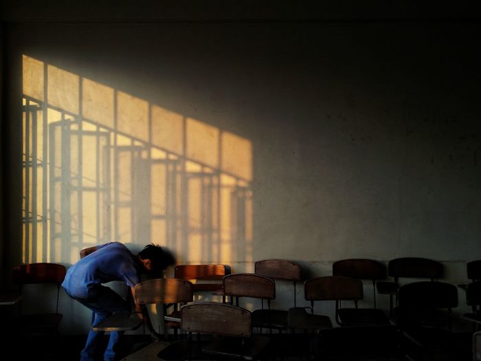 Rear view of man bending by wooden chairs in old lecture hall