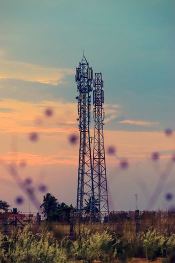 Communications tower on field against sky during sunset