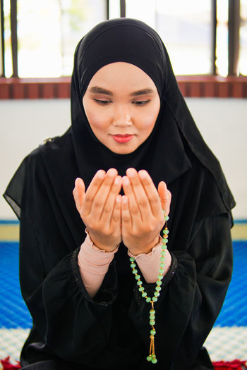 Young woman praying with beads while sitting at religious place