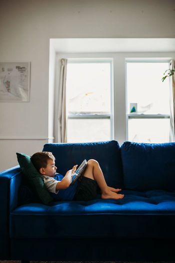 Preschool age boy laying on blue couch using tablet to learn