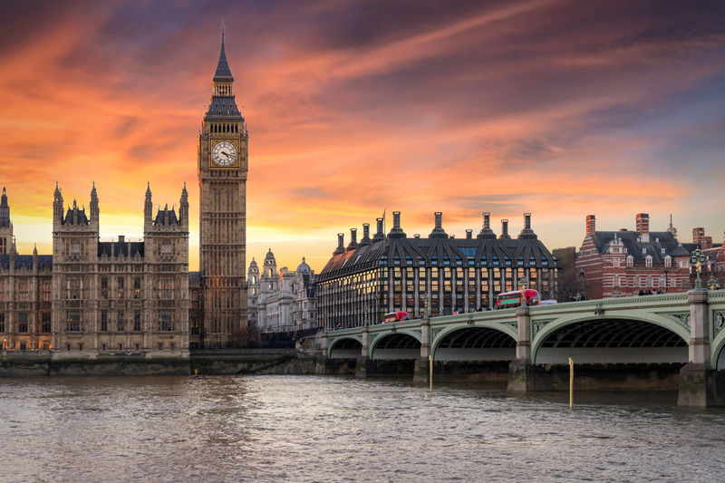 Westminster bridge over thames river by big ben against cloudy sky during sunset in city
