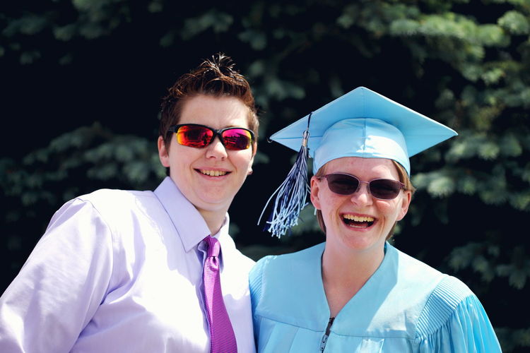 Portrait of happy graduate wearing mortarboard with lesbian friend