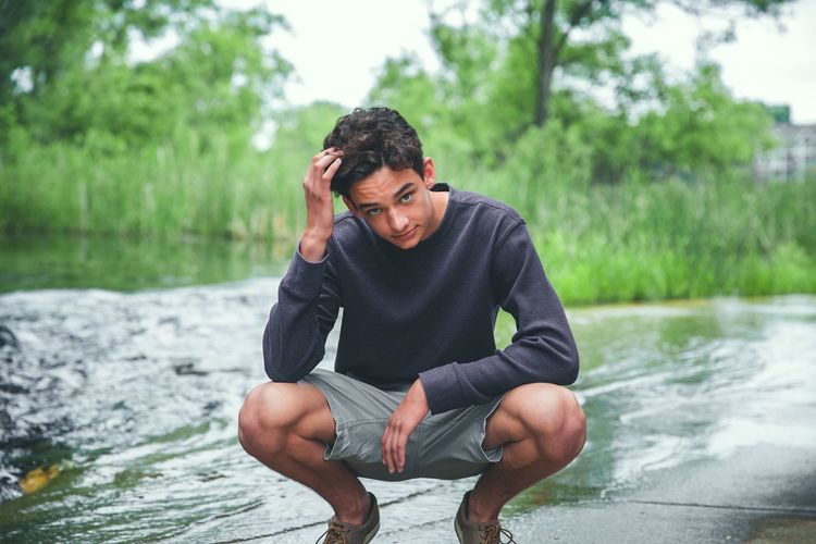 Teenage boy sitting by lake on road against trees