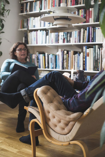 Female therapist talking to mature man by bookshelf at home office