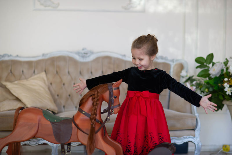 Beautiful little girl with a toy wooden horse in a vintage studio.
