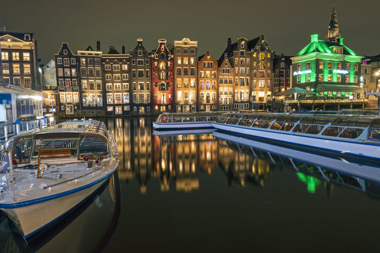 Traditonal houses and cruise boats at the damrak in amsterdam in the netherlands by night