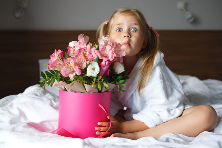 Portrait of girl sitting on bed with bouquet
