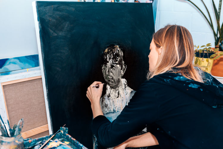 Female artist painting contemporary portrait on canvas inside atelier studio