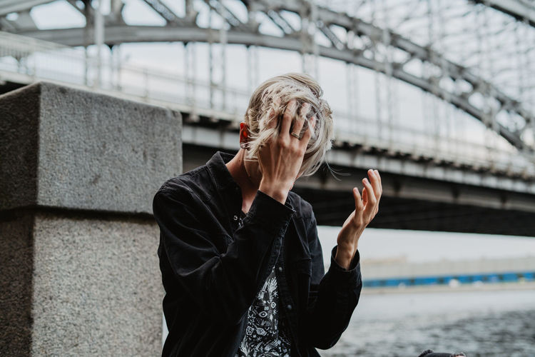 Man with hand in hair standing against bridge
