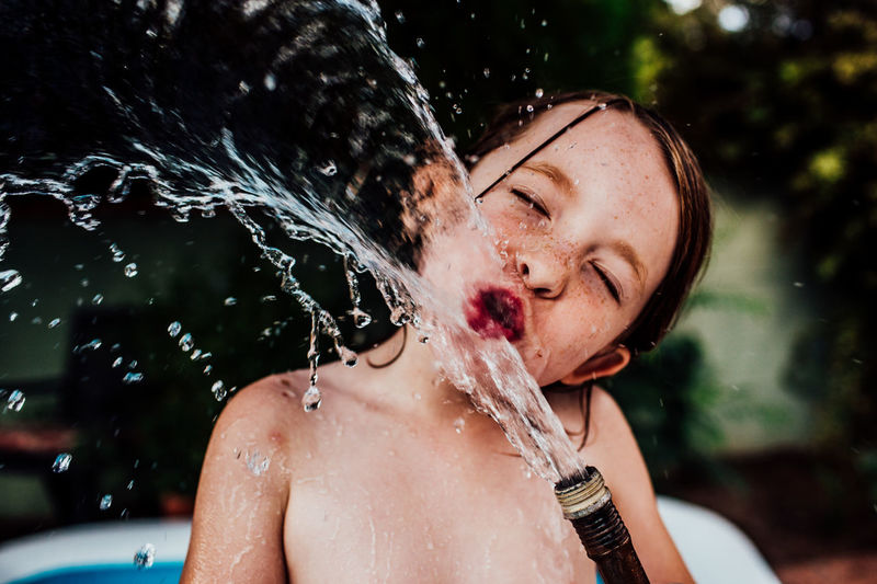 Young child drinking from a splashing hose outside in summer
