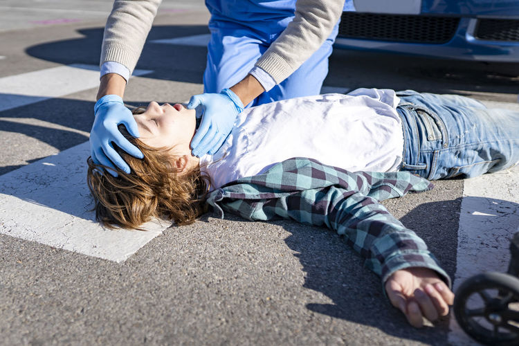 Doctor checking unconscious boy lying on road after car accident