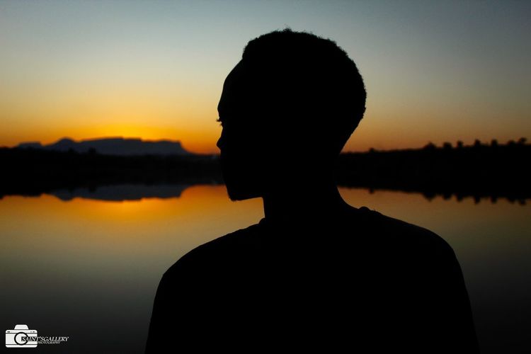 Portrait of silhouette man standing by lake against sky during sunset