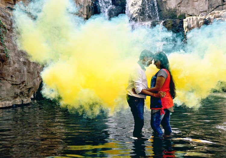 Side view of young couple standing amidst yellow smoke in lake
